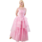 Lady with blonde hair, wearing the Glinda Wicked costume, standing with hands behind her back, smiling and looking forward, without the tiara. The shimmering pink bodice and cascading tulle skirt are clearly visible, against a white background