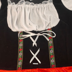 A woman modeling a traditional German dirndl costume against a plain white background. The costume features a black lace-up bodice with white puffed sleeves, a red skirt with white lace trim, white thigh-high stockings, and black Mary Jane heels.