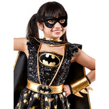A young girl wearing a black and gold sequined Batman costume with a matching black mask, cape, and metallic gold arm cuff, photographed against a plain white background.