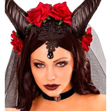 A woman wearing a devil costume headpiece with black horns, red roses, a black lace headband with a teardrop ornament, a black choker, and a sheer veil against a white background.