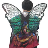 A person shown from the back wearing a large butterfly-shaped costume backpiece over a colorful printed shirt. The wings are black with iridescent green and blue sections and a fantasy character graphic printed on the center.