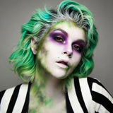 Person with green and gray hair and colorful makeup wearing a black and white striped shirt.