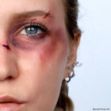 Close-up of a person's face with dramatic makeup and injuries on a plain background