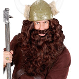 A man wearing a Viking costume accessory set, featuring a long brown curly wig, a green horned helmet with faux fur, and a brown tunic, holding a staff against a white background.