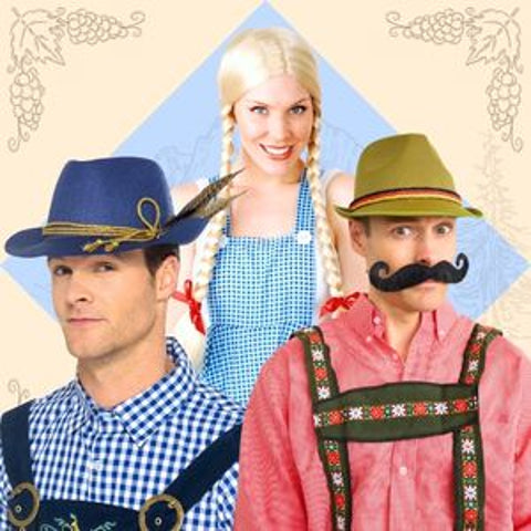 Three people wearing traditional Bavarian-style costumes posed together against a decorative cream background with grapevine motifs. One man wears a blue hat and blue-and-white gingham overalls, a woman wears a blue-and-white gingham apron, and another man wears a green hat, pink shirt, and embroidered suspenders.