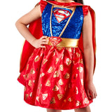 A child wearing a Supergirl costume dress with a blue sequined bodice, red skirt with gold S-shapes, and a red cape, shown against a plain white background.