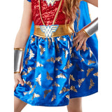 A child wearing a Wonder Woman costume dress with a red sequined bodice, blue skirt with gold logos, and a blue cape, shown against a plain white background.